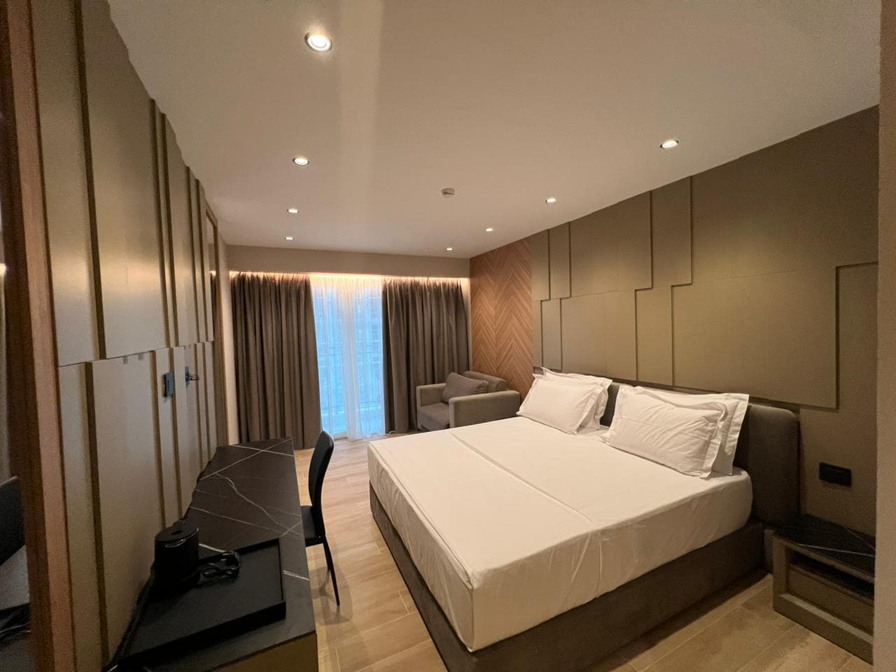 Bedroom with layered taupe panels, walnut details and a dark stone desk